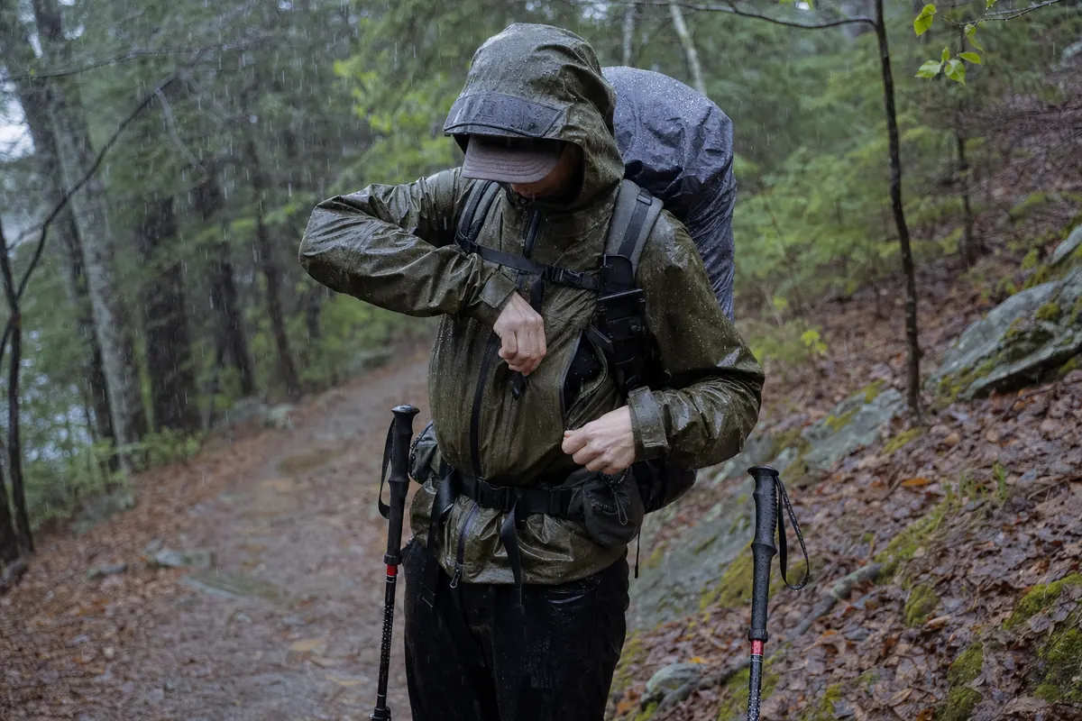 Rainy backpackers moving toward camp with wet shelter accessible outside a sealed dry core and conservative footing on a generic trail - rain backpacking system | KnowOutdoor