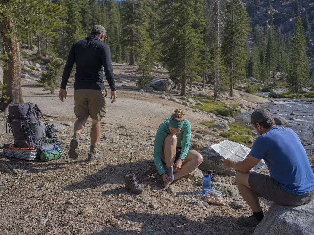 Backpacking group checking gait, feet, food, water, warmth, and the next map landmark during a planned stop