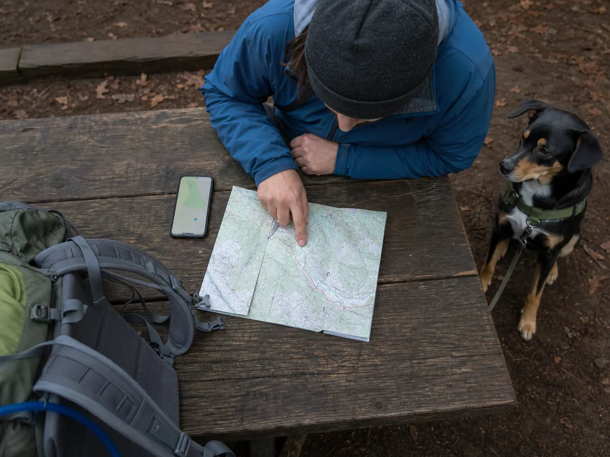 Handler tracing a generic backpacking route between trailhead, camp, water point, and exit while checking dog access notes - dog route rule map | KnowOutdoor