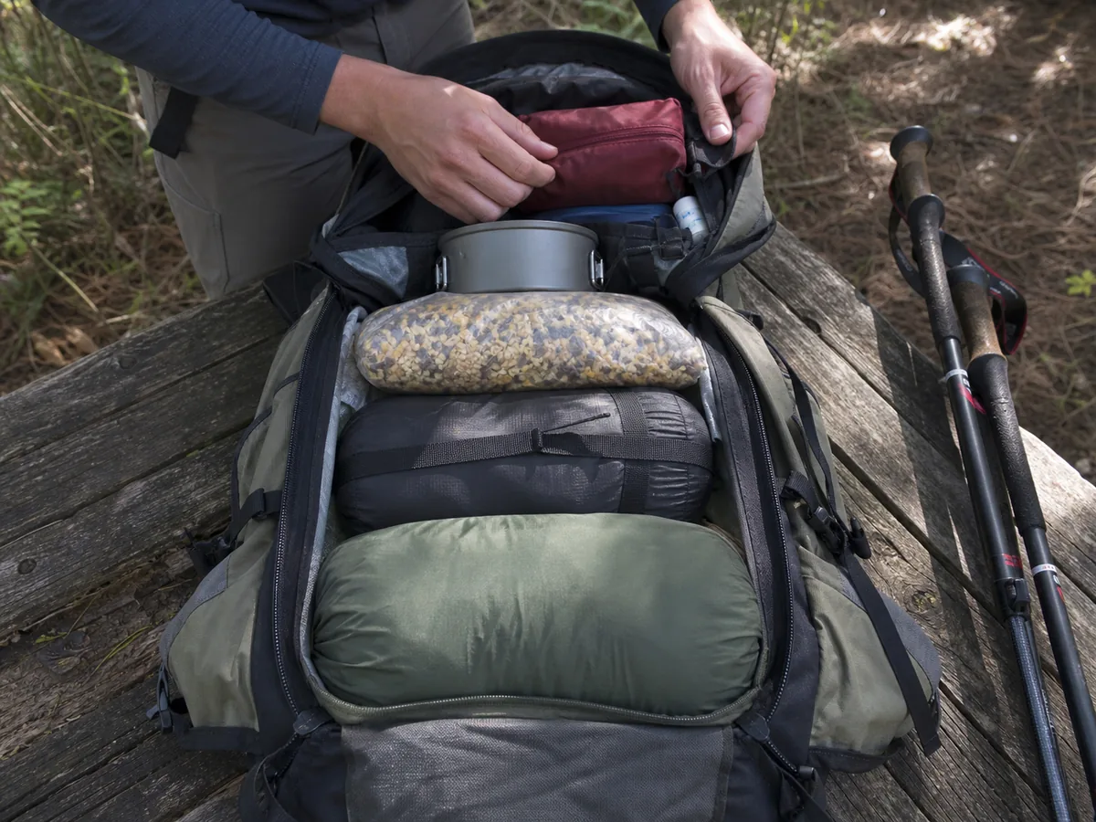 Backpacking gear arranged into soft bottom dense middle close to the spine and accessible top zones beside an open pack - backpack loading zones | KnowOutdoor