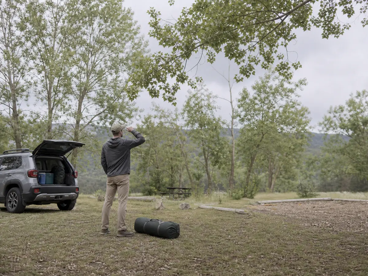 Camper checking wind direction and overhead branches before opening a tent bag - wind pitch site check | KnowOutdoor