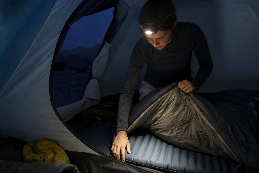 Camper checking pad alignment and sleeping bag dryness under a headlamp - cold-night sleep diagnosis | KnowOutdoor