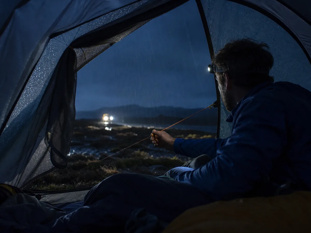 Solo camper checking rain and guyline tension safely from inside the tent at night - campsite night signals | KnowOutdoor