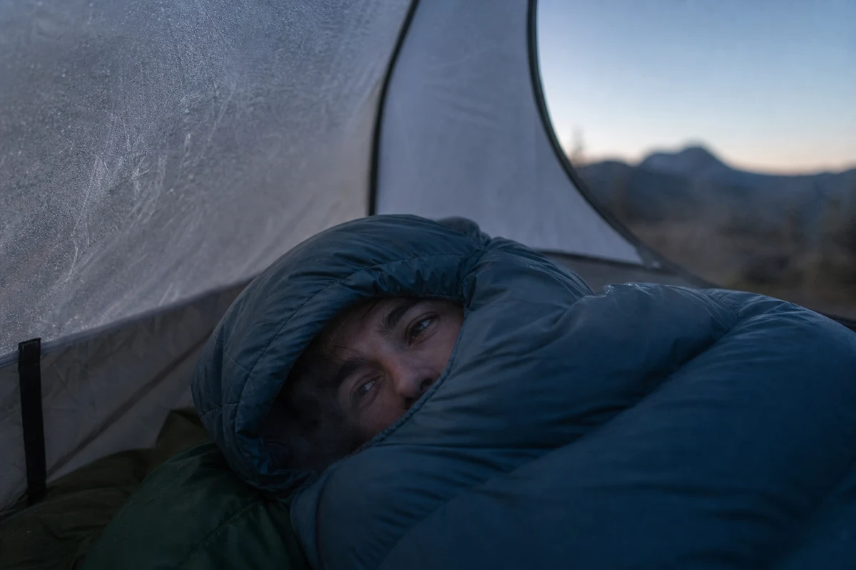 A camper cinched into a mummy sleeping bag hood inside a frosted tent at dawn - Sleeping bag temperature rating in cold conditions | KnowOutdoor