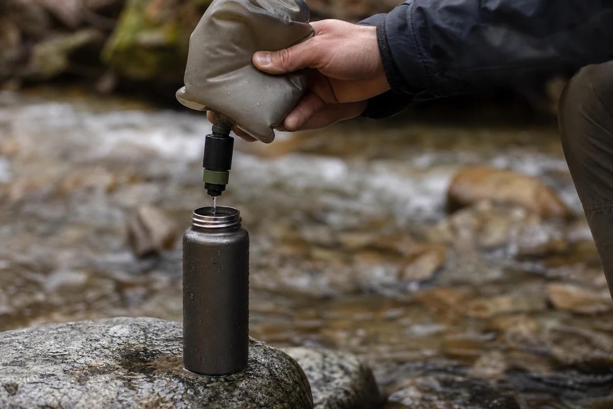 A hiker squeezing water through a soft-flask filter into a bottle at a stream - Filtering flow rate and clogging in the field | KnowOutdoor