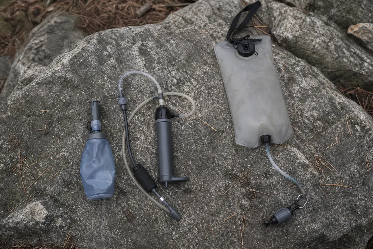 A squeeze filter, a pump filter, and a gravity filter bag laid out on a flat rock - Backcountry water filter types compared | KnowOutdoor