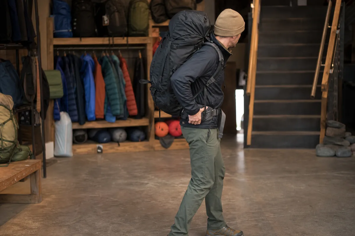 Hiker walking with a fully loaded pack, a hand on the hipbelt, testing the fit - Loaded fit test | KnowOutdoor