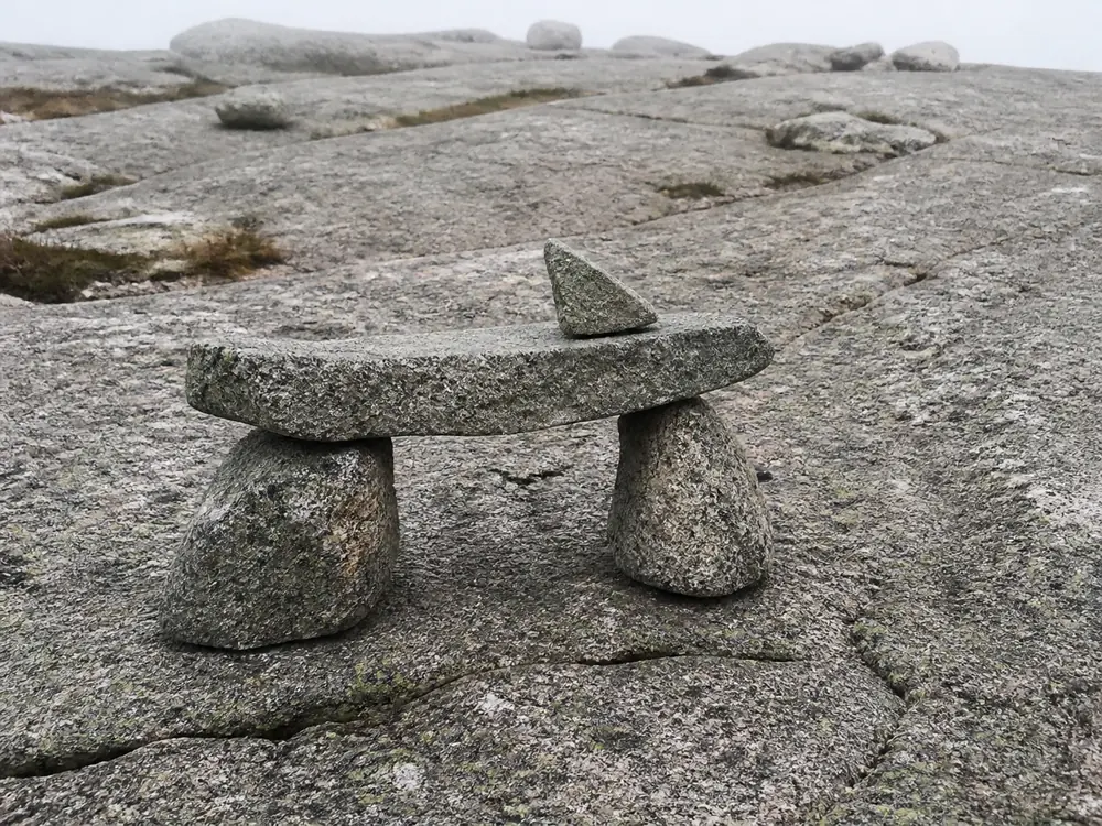 Bates-style cairn with two base stones, a flat lintel, and a pointer stone on bare rock