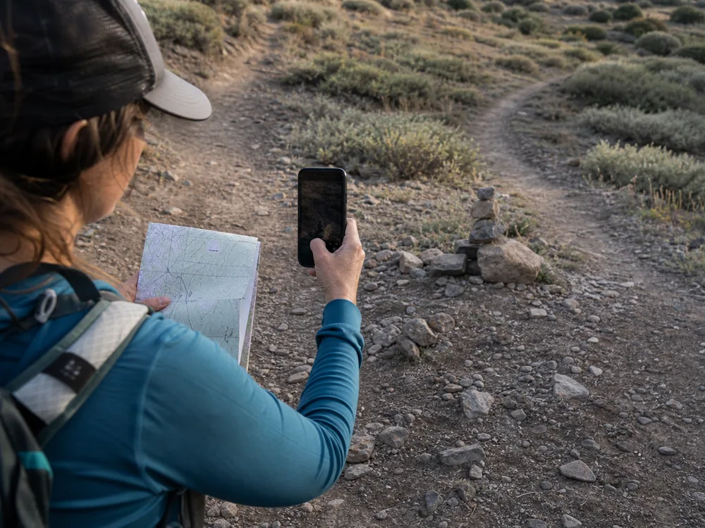 Hiker photographs a questionable rock stack from the trail while holding a topographic map