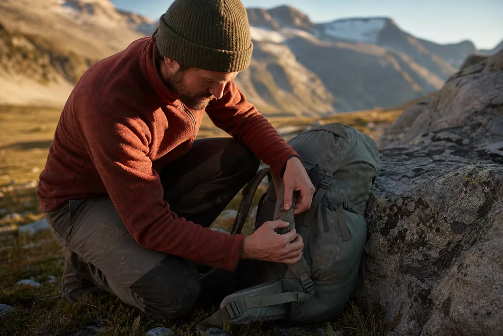 A hiker crouched beside a rock tightening the hipbelt of a faded daypack - adjustment before replacement - KnowOutdoor