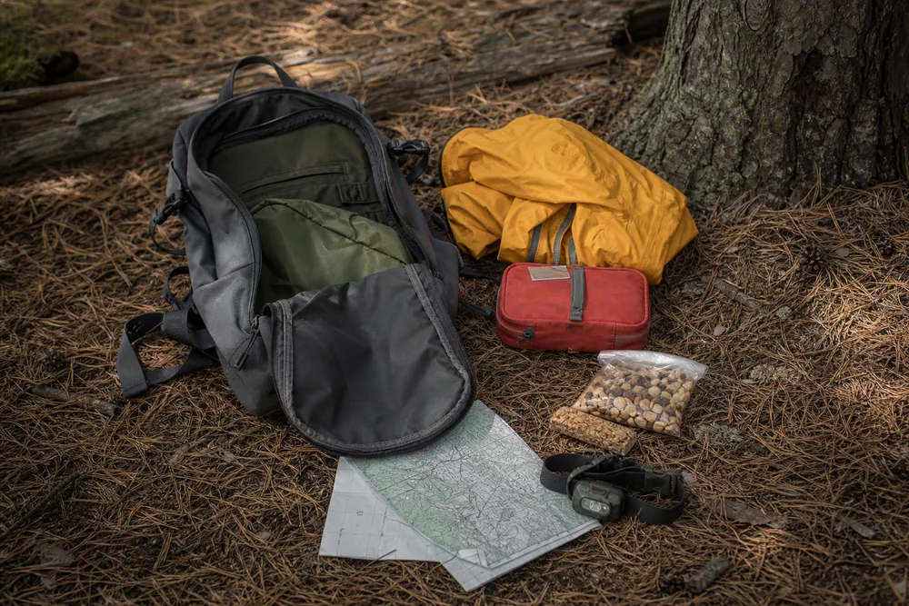 A small daypack opened with its contents laid beside it on pine needles - day hiking gear - KnowOutdoor