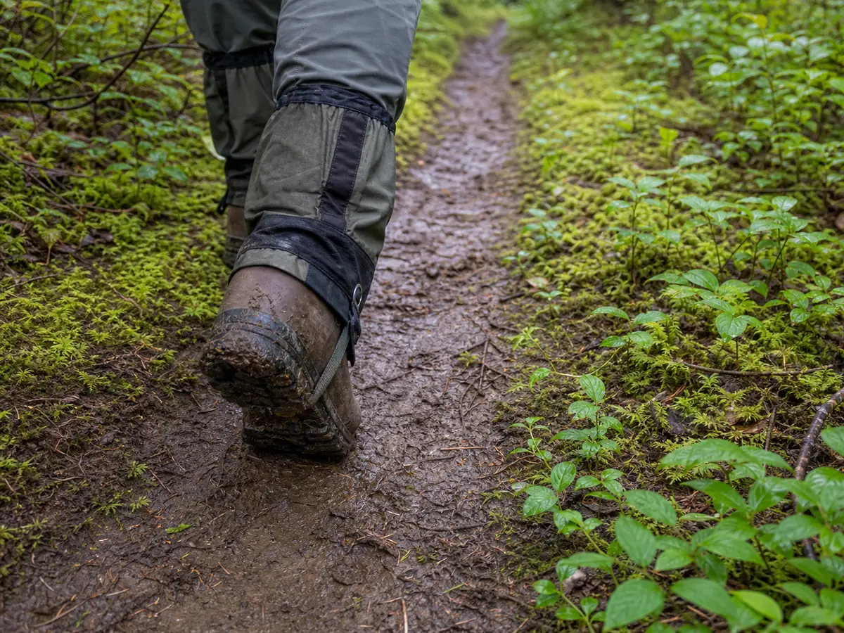 Hiker staying on the firm center of a muddy trail instead of widening the planted edge