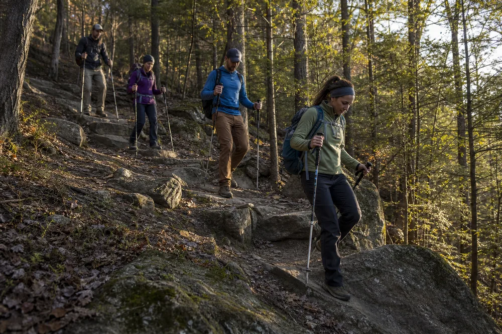 Four hikers leaving safe stopping space between each person on a rocky forest descent