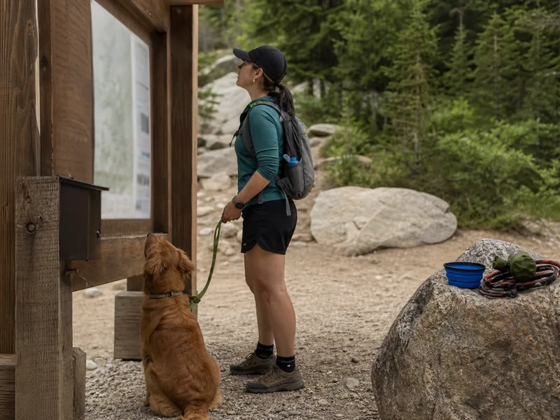 Hiker checking dog trail rules with leash and water bowl at a trailhead