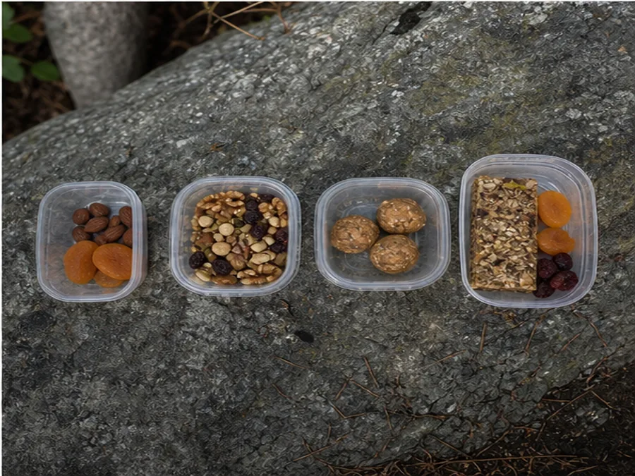Day hike snacks in small plain containers arranged on a rock - how to fuel and snack on a day hike | KnowOutdoor