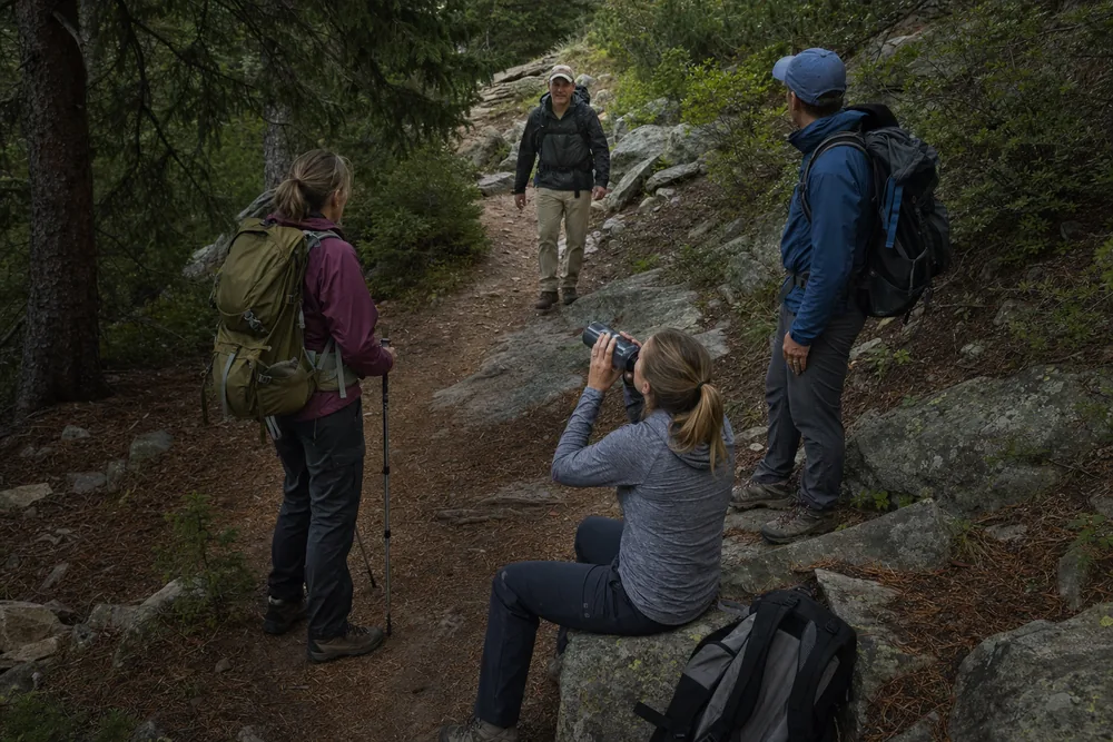Four hikers gathered at a shaded bend in a mountain trail during a short regroup stop with one just arriving - group hiking regroup point | KnowOutdoor