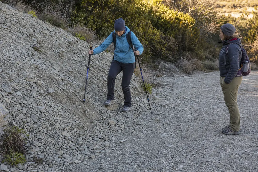 Hiker practicing short controlled steps on a low gravel patch beside stable ground before an exposed loose-rock section