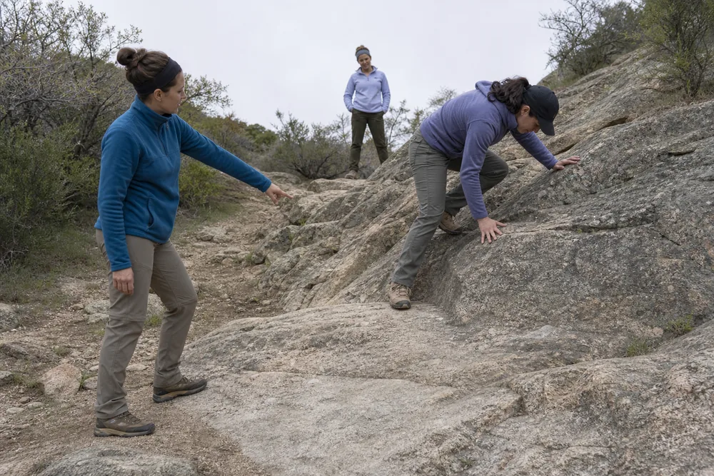 One hiking partner calmly guiding another back toward a broad stable stance on low rock while the group stays clear