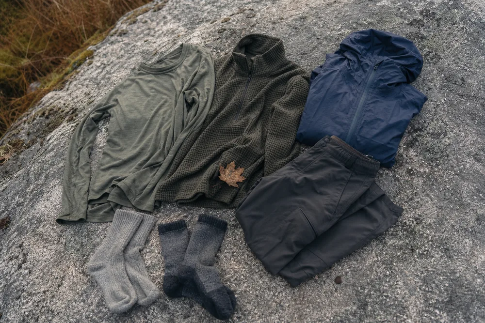 Hiking layers laid out on rock showing base layer, mid layer, and weather shell - what to wear hiking | KnowOutdoor