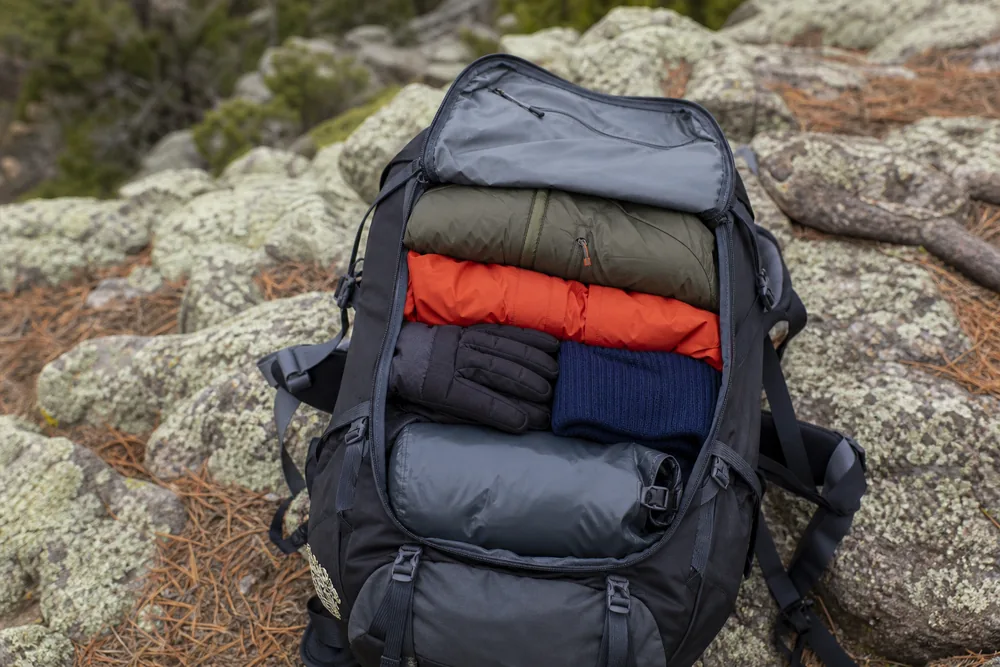 Open trekking pack shows weather shell, insulated jacket, gloves, and hat in a fast-access layer above dry camp clothing - Layer access order | KnowOutdoor
