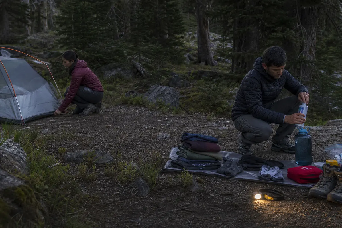 Two trekkers timing shelter setup, water treatment, dry layers, and foot care at a practice camp - camp routine rehearsal | KnowOutdoor