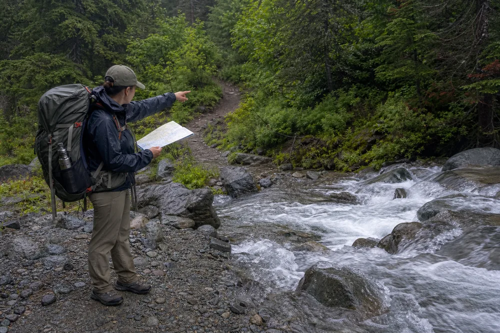 Solo trekker stopping on a stable bank before a fast unbridged creek and checking an alternate route