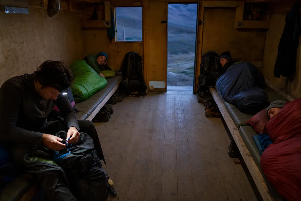 Trekkers keeping packs compact and a clear walkway inside a simple backcountry shelter - trekking etiquette shared shelter | KnowOutdoor