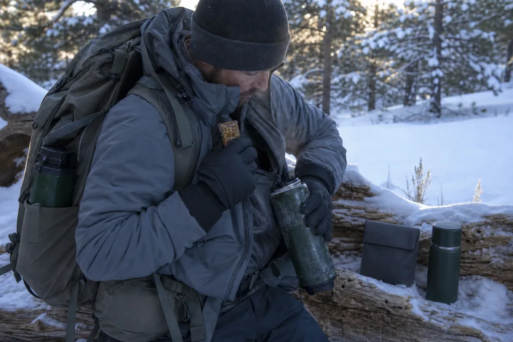 Winter trekker checking an insulated water bottle and soft ready-to-eat food while wearing gloves