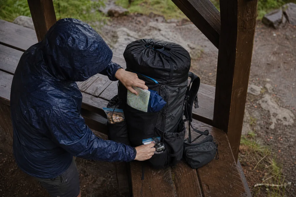 Trekker placing a rain shell, map, snack, headlamp, and blister care in reachable backpack pockets